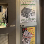 Porta esterna del bagno dell'ufficio con manifesto per la Caritas Diocesana di Siena