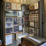 Angolo cornici varie con le opere di "Aqua" e raccoglitore a schede sul tavolo per le riunioni