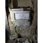 dall'alto: nicchia che ospitava il busto di San Bernardino, sotto due lapidi tradotte nell'articolo e più in bassoi cocci a terra, tra cui i resti del busto di San Bernardino